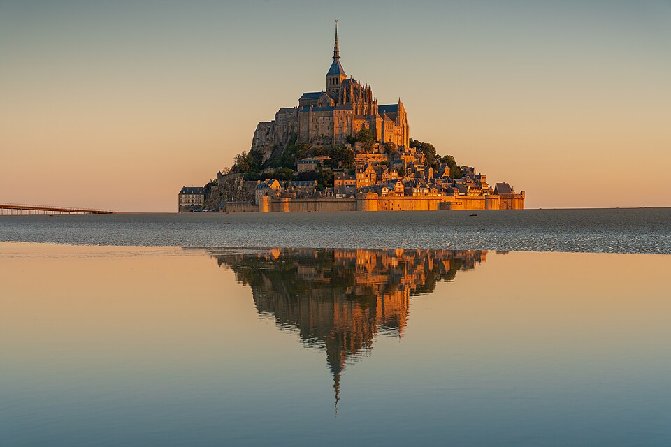 Le Mont-Saint-Michel, monument de Bâtisseurs médiévaux anonymes : Une abbaye couronne un îlot rocheux entouré par la baie, avec des remparts et…