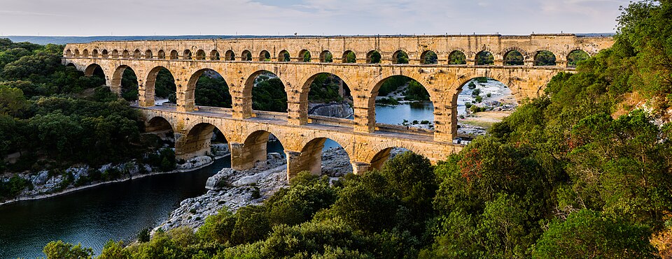 Le Pont du Gard, monument de Ingénieurs romains anonymes : Un aqueduc monumental à trois niveaux d’arches traverse une vallée au-dessus du…