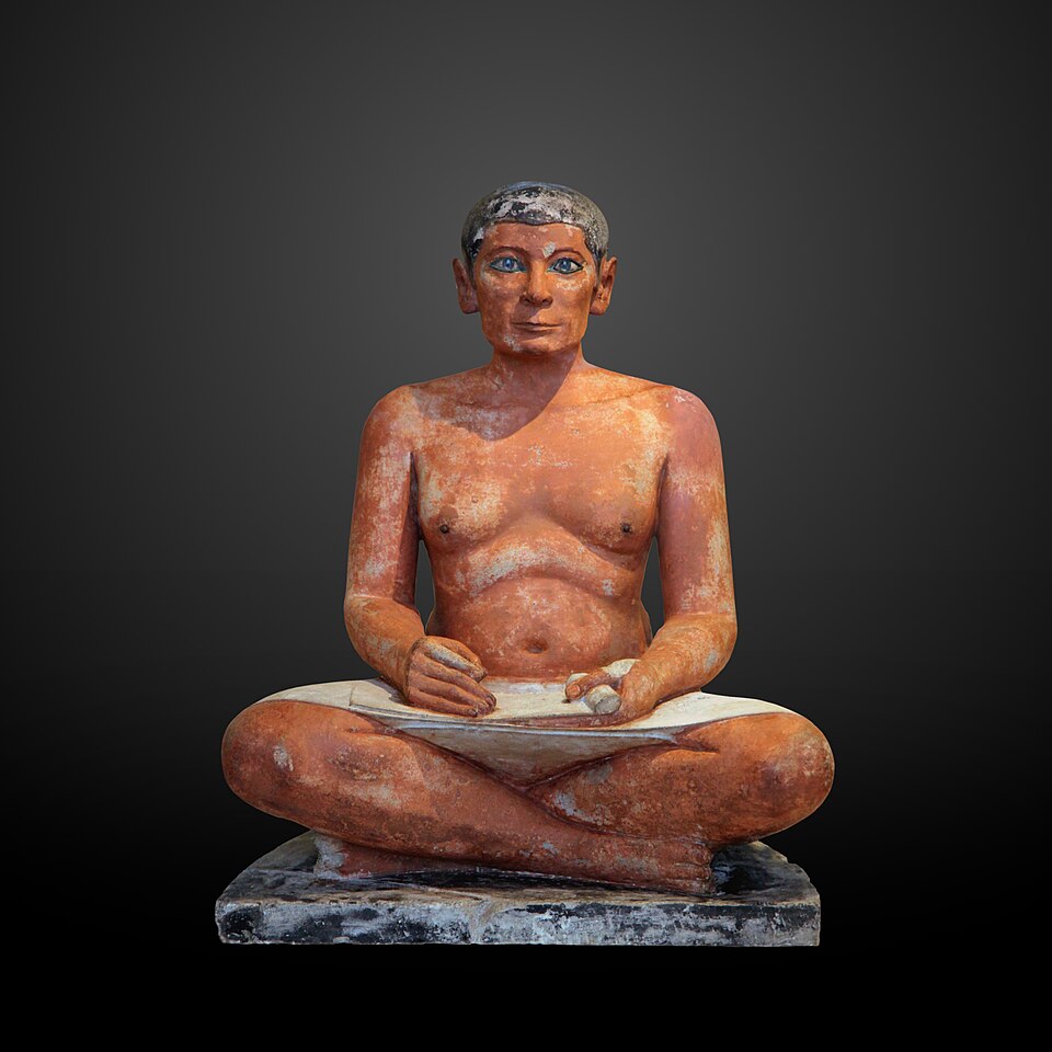 Le Scribe accroupi, sculpture de Sculpteur égyptien anonyme : Un homme assis jambes croisées tient un rouleau, avec de grands yeux incrustés qui…